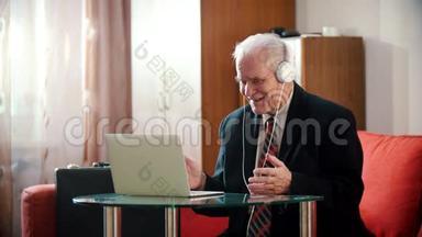 <strong>年迈</strong>的祖父-戴着耳机的老祖父微笑着看着房间里的笔记本电脑屏幕